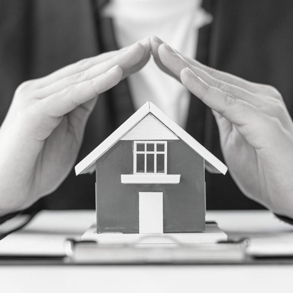 Close-up of a small model house being pinched between two fingers, in grayscale photo