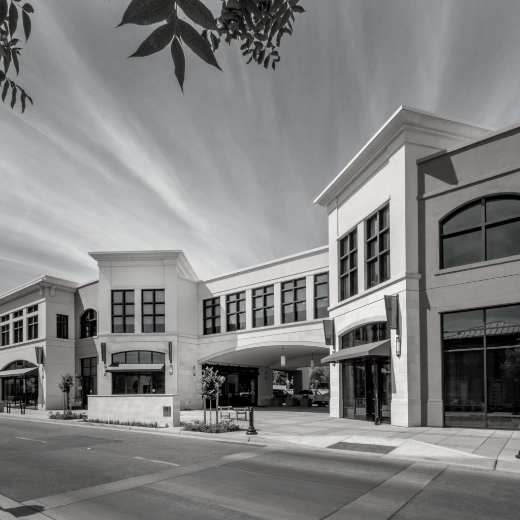 Modern white stone office building with large grid windows and a curved entrance, along a street (black-and-white).