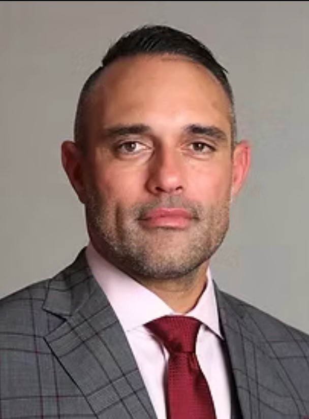 Professional headshot of a man in a gray plaid suit and red tie, posing against a neutral background.